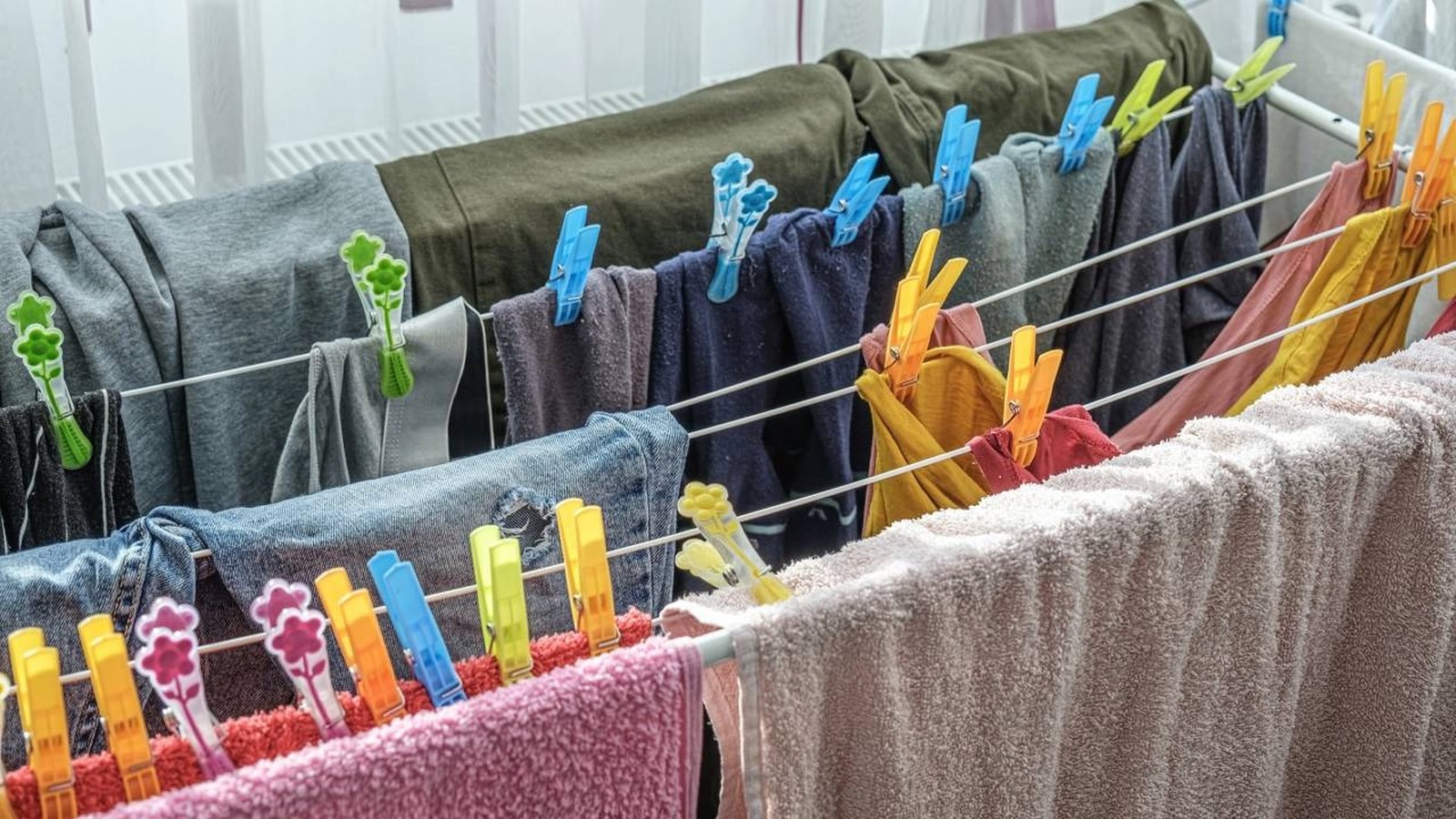 Varal de chão com roupas coloridas e toalhas penduradas e presas por prendedores em ambiente interno