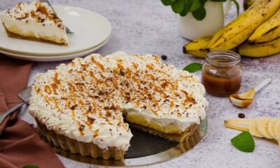 Torta banoffee inteira com fatia removida, bananas, calda de caramelo e menta em mesa
