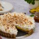 Torta banoffee inteira com fatia removida, bananas, calda de caramelo e menta em mesa