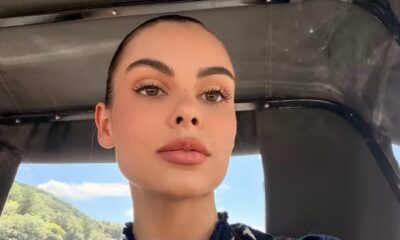 Rosto de Amanda Kimberlly em close, olhos castanhos, lábios rosados, com paisagem externa ao fundo