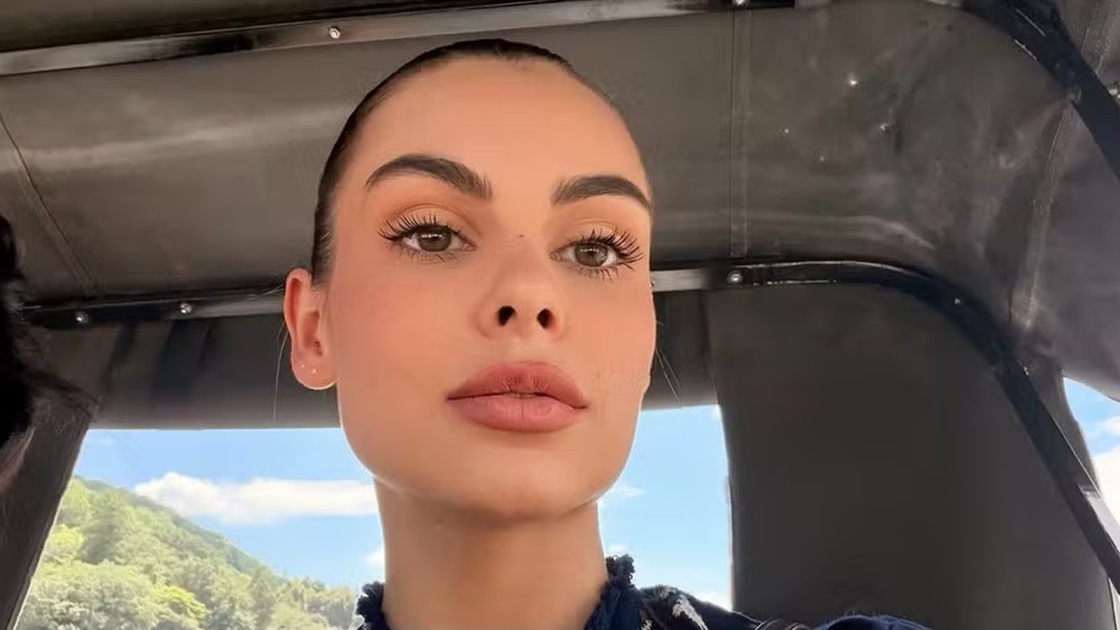 Rosto de Amanda Kimberlly em close, olhos castanhos, lábios rosados, com paisagem externa ao fundo