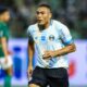 Jogador Carlos Vinícius em campo com camisa listrada azul e branca do Grêmio e shorts pretos