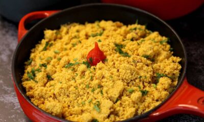 Panela de ferro vermelha com farofa amarela, salpicada com cheiro-verde e uma pimenta vermelha