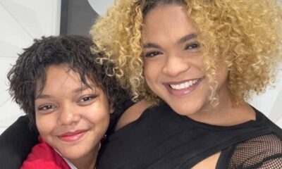 Duas jovens sorridentes, uma com cabelo crespo escuro, outra com cabelo crespo loiro, se abraçando