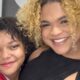 Duas jovens sorridentes, uma com cabelo crespo escuro, outra com cabelo crespo loiro, se abraçando