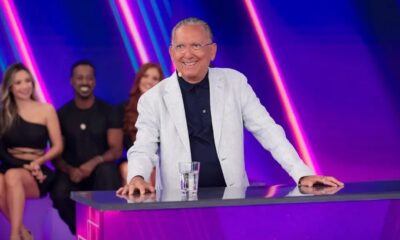 Galvão Bueno sorridente em estúdio, com blazer, atrás de balcão com copo
