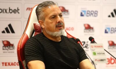 Homem com cabelo grisalho e barba, José Boto, sentado, falando em microfones, com logos ao fundo