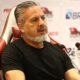 Homem com cabelo grisalho e barba, José Boto, sentado, falando em microfones, com logos ao fundo