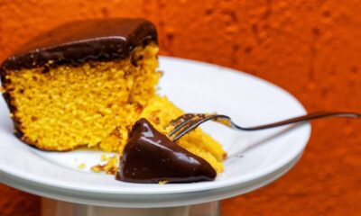 Fatia de bolo de cenoura com cobertura de chocolate derretida em prato branco com garfo