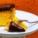 Fatia de bolo de cenoura com cobertura de chocolate derretida em prato branco com garfo