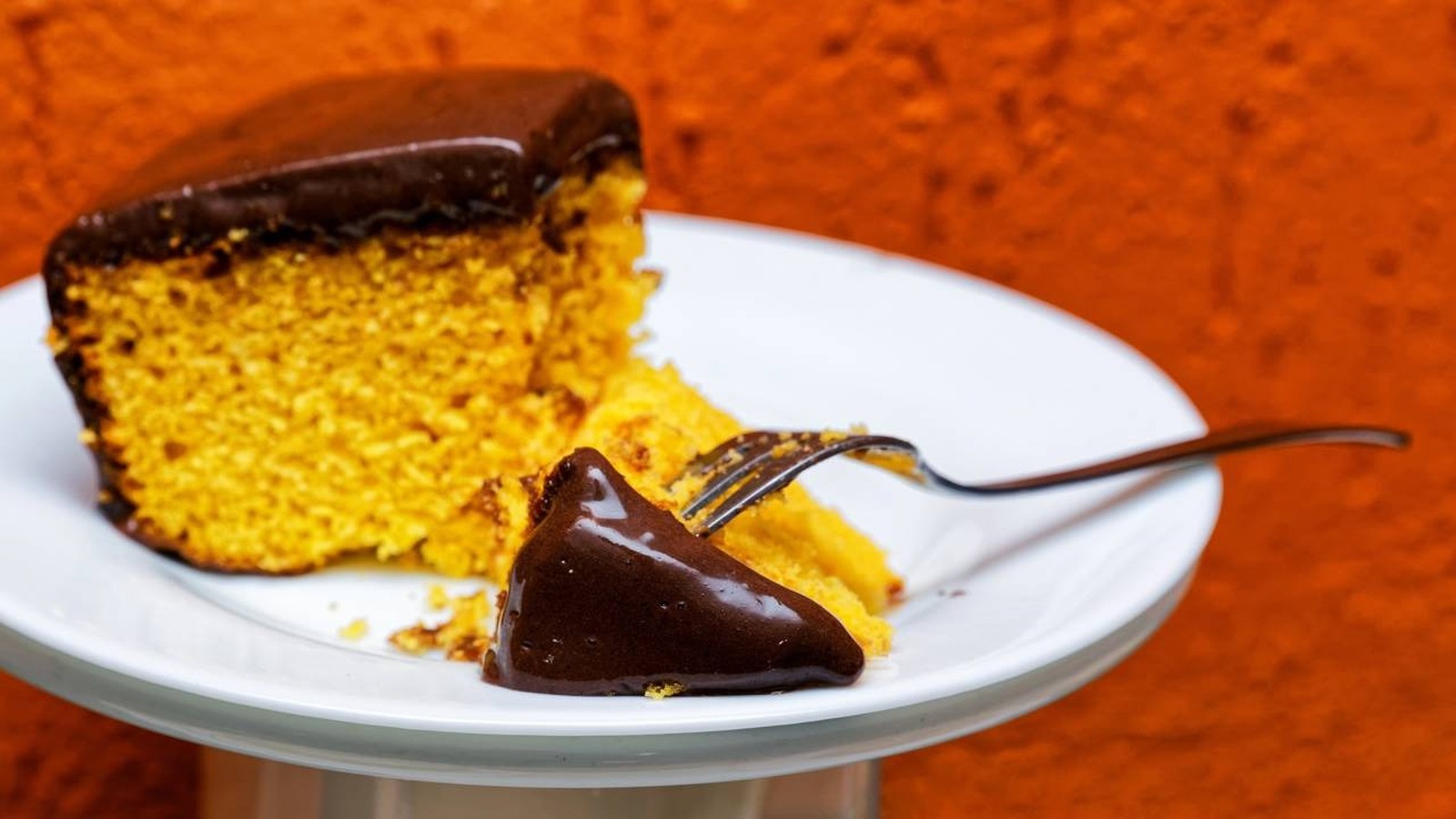 Fatia de bolo de cenoura com cobertura de chocolate derretida em prato branco com garfo