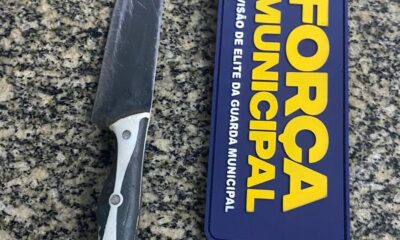 Faca com cabo preto e branco ao lado de distintivo azul com texto Força Municipal