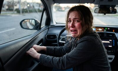 Mulher jovem chora intensamente no banco do motorista de um carro, agarrando a maçaneta da porta