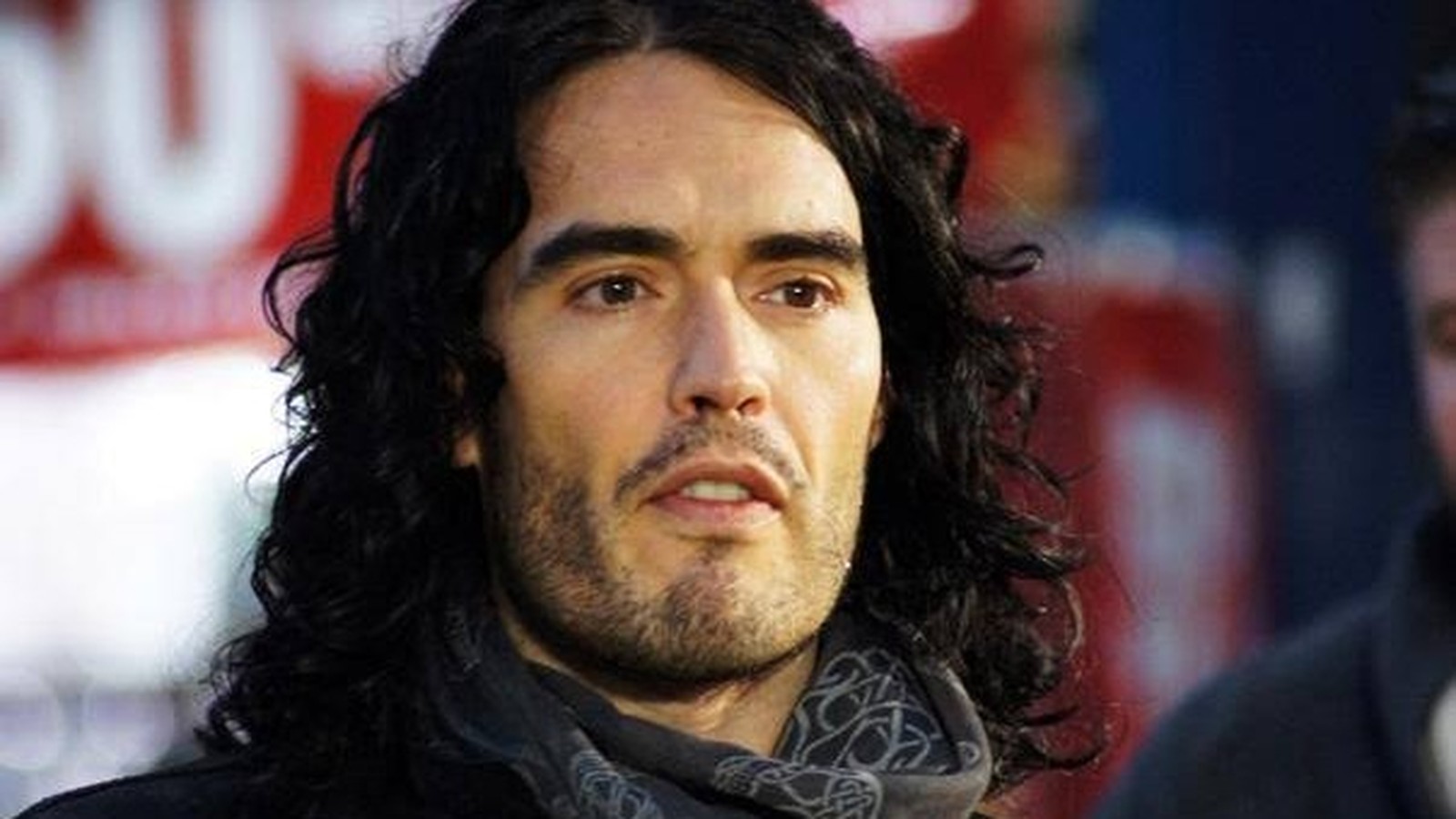 Retrato de Russell Brand com cabelo comprido e escuro, barba e expressão séria