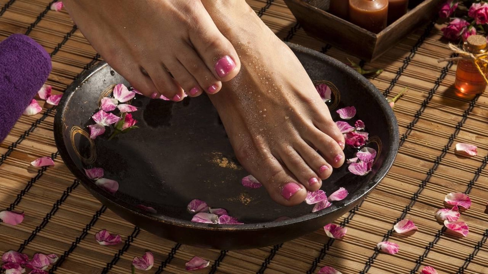 Pés de uma pessoa imersos em bacia escura com água e pétalas de rosa em bambu