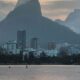 Pessoas em stand-up paddle em lago. Skyline urbano, montanhas ao fundo, céu nublado