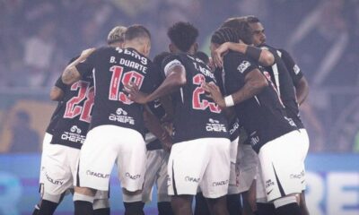 Jogadores de futebol de uniforme preto e branco com logos 'Moto Chefe' e 'Facility' huddle em campo