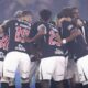 Jogadores de futebol de uniforme preto e branco com logos 'Moto Chefe' e 'Facility' huddle em campo