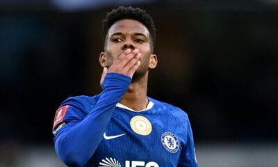 Jovem jogador de futebol, Estêvão, em camisa azul do Chelsea, soprando um beijo em campo