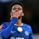 Jovem jogador de futebol, Estêvão, em camisa azul do Chelsea, soprando um beijo em campo