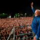Presidente Lula no palco, acenando para uma vasta multidão com celulares acesos, à noite