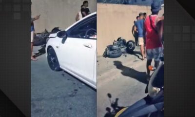 Carro branco e motocicleta danificada no chão após acidente com pessoas ao redor