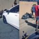 Carro branco e motocicleta danificada no chão após acidente com pessoas ao redor