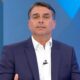 Homem de terno azul, camisa branca, em estúdio de TV azul, olhando à frente