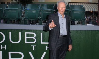 Clint Eastwood, terno xadrez, camisa cinza, apontando. Fundo: letras "DUBL HTH IDV", assentos