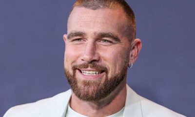 Close-up de Travis Kelce sorrindo com barba, cabelo curto e brinco