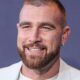 Close-up de Travis Kelce sorrindo com barba, cabelo curto e brinco