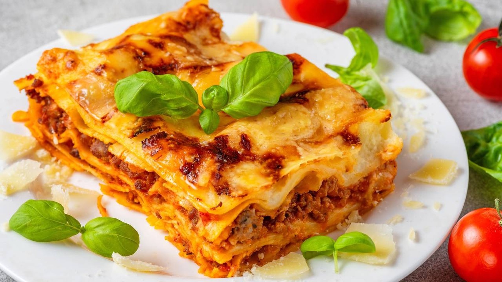 Close-up de uma porção de lasanha em prato branco, guarnecida com manjericão e queijo parmesão