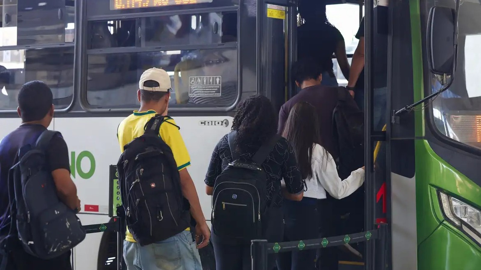 Pessoas com mochilas embarcam em um ônibus público verde e branco