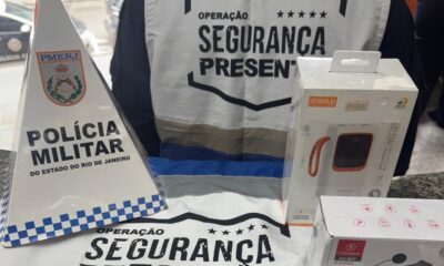 Sinal Polícia Militar, banner Segurança Presente, caixas α GOLD power bank e Kapboom fone