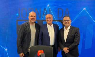 Três homens sorrindo em estúdio de rádio azul com logo "Jornal da Tupi" e "tupi 98"