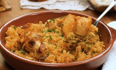 Galinhada em travessa marrom com frango, arroz e salsa, sendo servida por um garfo