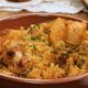Galinhada em travessa marrom com frango, arroz e salsa, sendo servida por um garfo