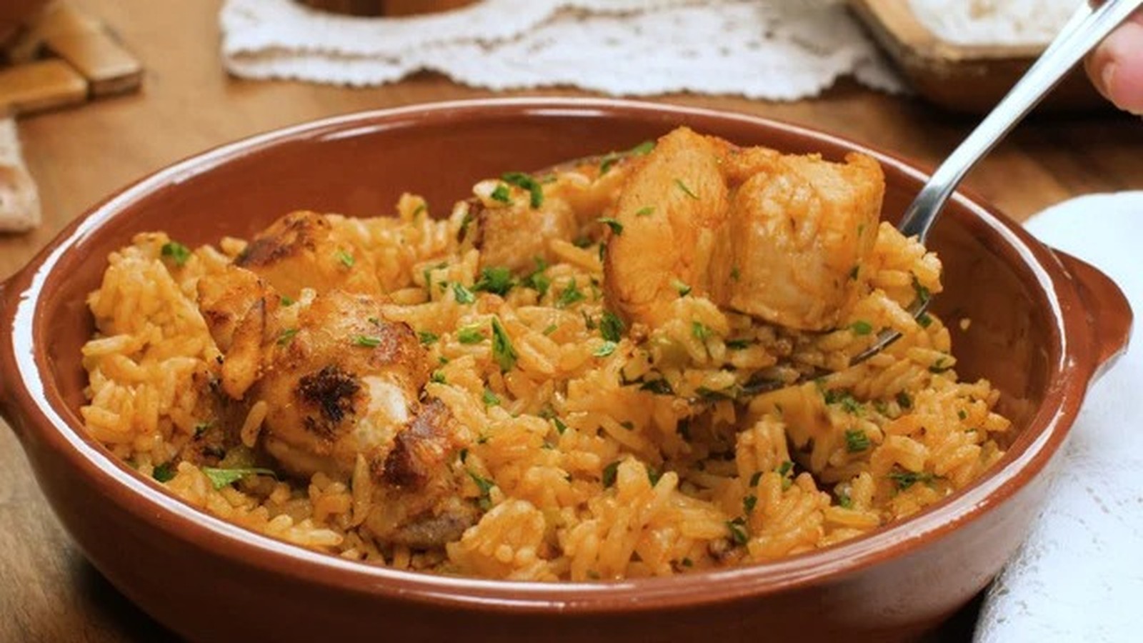 Galinhada em travessa marrom com frango, arroz e salsa, sendo servida por um garfo