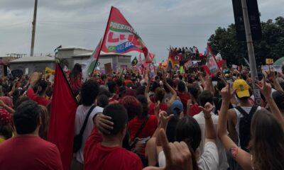Multidão em ato político, com bandeira vermelha escrita "PRESIDENTE LULA", pessoas fazendo "L" com as mãos