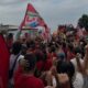 Multidão em ato político, com bandeira vermelha escrita "PRESIDENTE LULA", pessoas fazendo "L" com as mãos