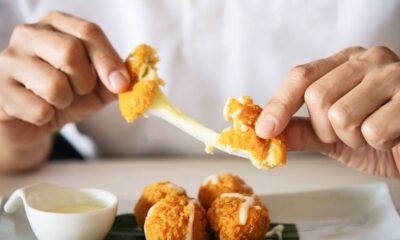 Duas mãos puxam uma bolinha de queijo, mostrando queijo derretido esticando, com mais bolinhas e molho