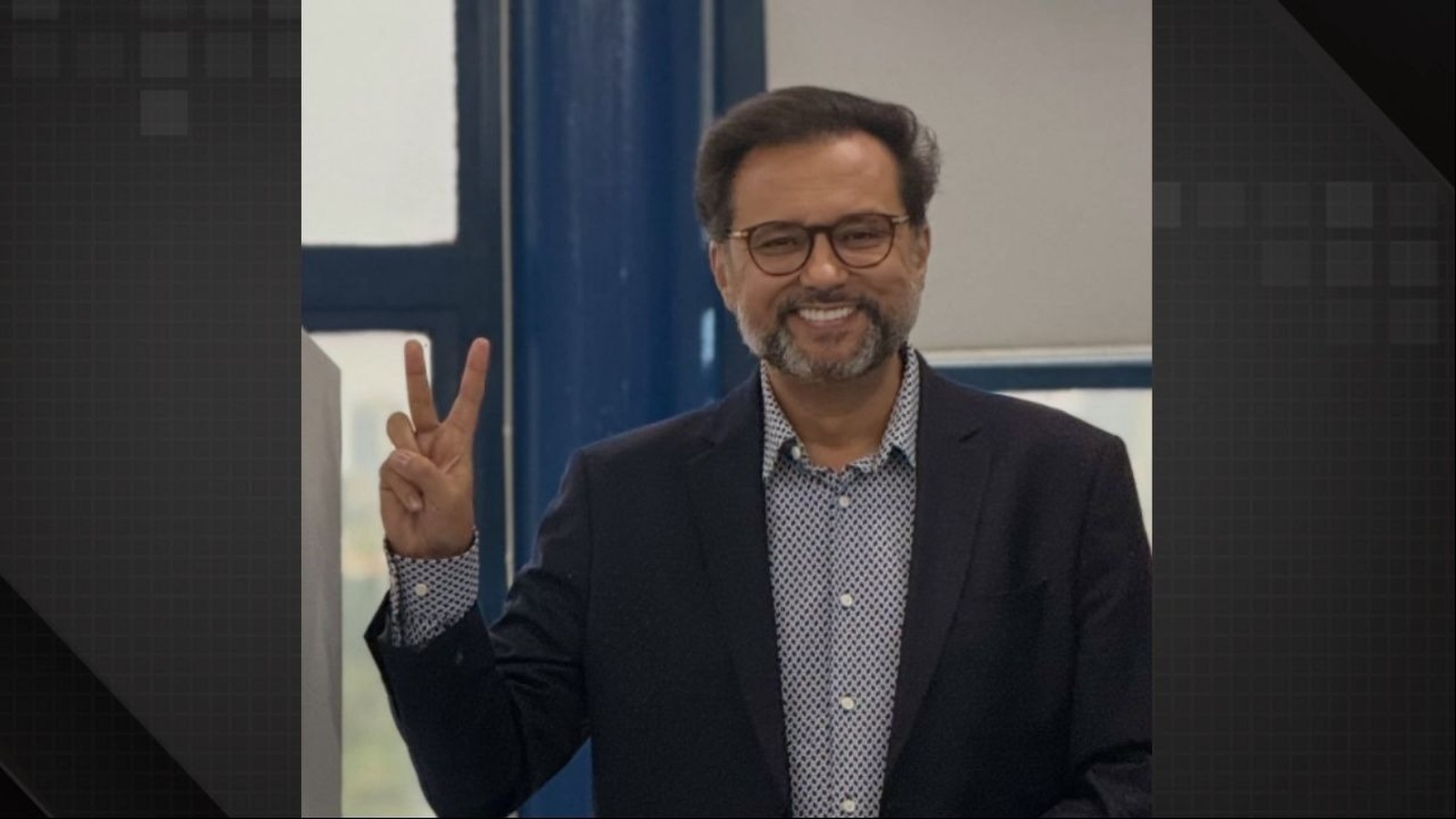 Geraldo Luís sorrindo, usando óculos e barba, fazendo sinal de paz com a mão direita