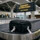Mala preta em esteira de bagagens de aeroporto internacional, representando caso de extravio que resultou em indenização de R$ 6 mil. - Imagem ilustrativa criada por inteligência artificial