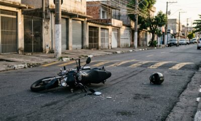 Motocicleta preta caída no asfalto próximo a uma lombada em avenida urbana, representando acidente durante corrida de moto por aplicativo. - Imagem ilustrativa criada por inteligência artificial