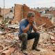 Homem de roupas simples chora diante dos escombros de uma casa de tijolos demolida, com paredes destruídas e entulhos espalhados em bairro popular de Goiânia. - Imagem ilustrativa criada por inteligência artificial