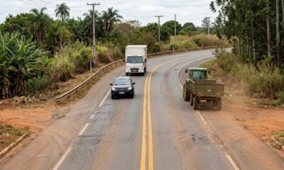 Carro preto ultrapassa trator verde em rodovia de pista simples com faixa dupla amarela contínua, enquanto caminhão se aproxima no sentido contrário. - Imagem ilustrativa criada por inteligência artificial