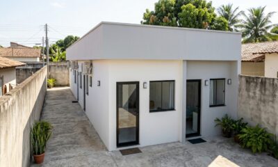 Duas kitnets térreas compactas com entradas independentes, fachadas brancas e cinzas e corredor de concreto em terreno residencial brasileiro. - Imagem ilustrativa criada por inteligência artificial