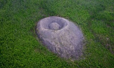 Visão aérea de um monte cônico rochoso cinzento com depressão central, em floresta verde densa