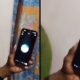Mulher segura smartphone de capa laranja, tela escura, com círculo azul e branco
