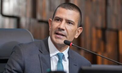 Homem de terno cinza e gravata azul fala em microfone em ambiente de tribunal